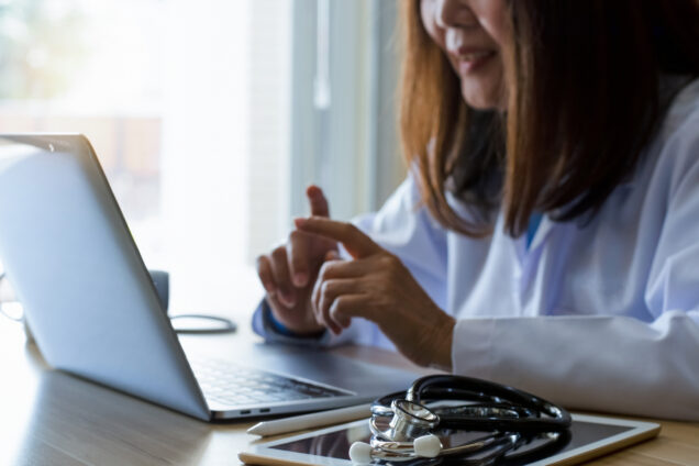 Doctor speaking with someone on her laptop while seated at a desk.